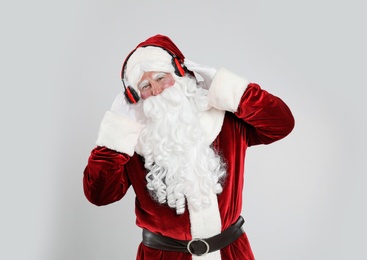 Santa Claus with headphones listening to Christmas music on light grey background