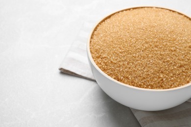 Brown sugar in bowl on light grey table, closeup. Space for text