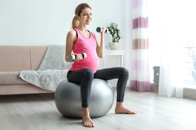 Young pregnant woman doing exercises with dumbbells at home
