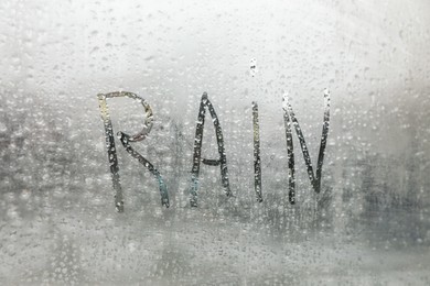 Word Rain written on foggy window, closeup view