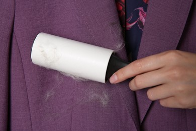 Photo of Woman removing hair from purple jacket with lint roller, closeup
