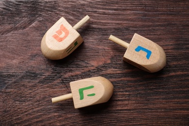 Hanukkah traditional dreidels with letters He, Pe and Nun on wooden table, flat lay