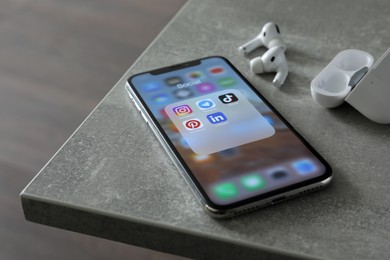 MYKOLAIV, UKRAINE - AUGUST 10, 2021: Apple iPhone X, AirPods and charging case on grey table. Screen with different social media icons