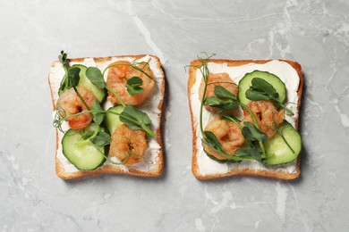 Tasty toasts with cream cheese, shrimps, cucumbers and microgreens on grey marble table, flat lay