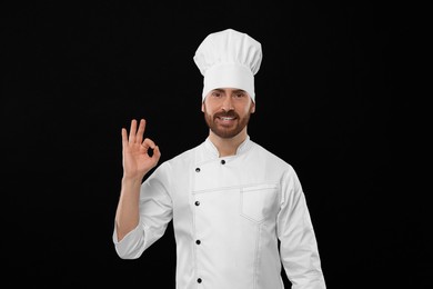 Photo of Smiling mature chef showing ok gesture on black background