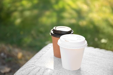 Photo of Cardboard cups with tasty coffee on stone bench outdoors. Space for text