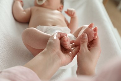 Photo of Mother massaging her cute baby with oil on changing table, closeup