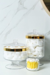Jars with cotton balls, swabs and pads on white countertop in bathroom