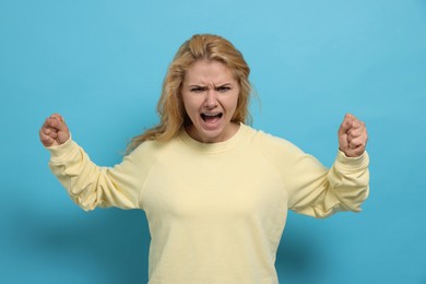 Photo of Aggressive young woman screaming with rage on light blue background