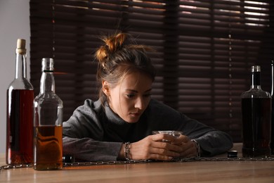Alcohol addiction. Woman chained with glass of liquor at wooden table in room