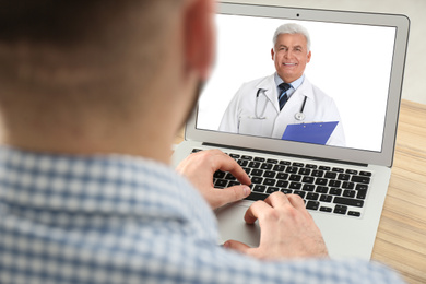 Image of Man using laptop at table for online consultation with doctor via video chat, closeup
