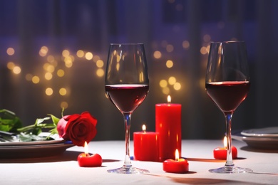 Beautiful table setting with glasses of wine, candles and rose against blurred lights. Romantic dinner for Valentine's day