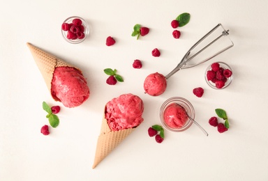Flat lay composition with delicious pink ice cream in wafer cones and raspberries on white table