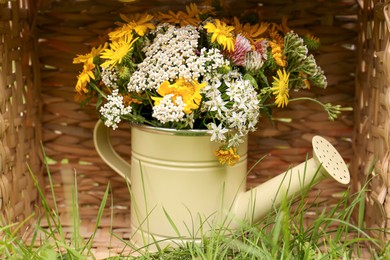 Photo of Pale yellow watering can with beautiful flowers in wicker box