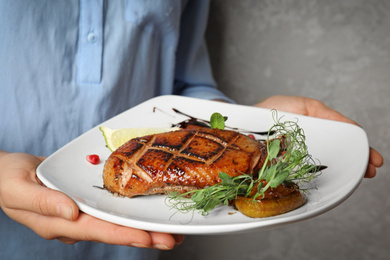 Photo of Woman holding plate with grilled duck breast on grey background, closeup