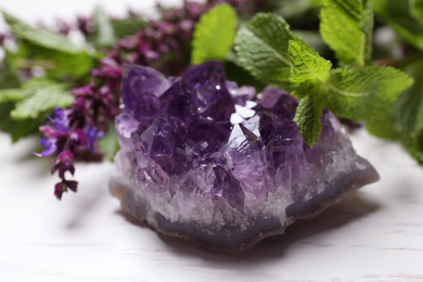Amethyst gemstone and healing herbs on white wooden table, closeup
