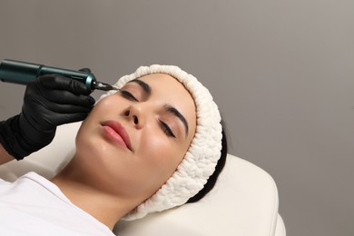 Photo of Young woman undergoing procedure of permanent eyeliner makeup on grey background, closeup