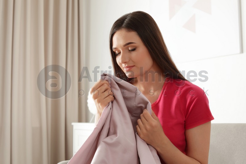 Young beautiful woman smelling fresh laundry indoors. Space for text