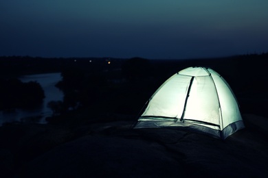 Small camping tent glowing in twilight outdoors. Space for text