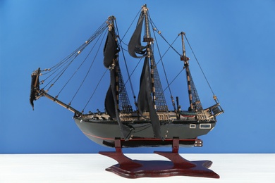 Miniature model of old ship with black sails on white table against blue background