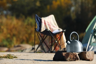 Metal kettle on rocks outdoors, space for text. Camping equipment