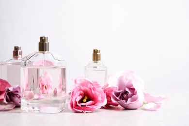 Bottles of perfume and beautiful flowers on light table. Space for text