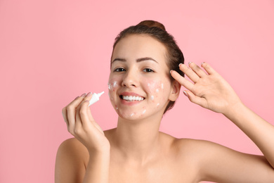 Teen girl with acne problem applying cream on light pink background