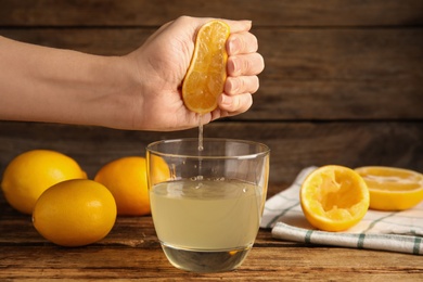 Woman squeezing lemon juice at wooden table, closeup