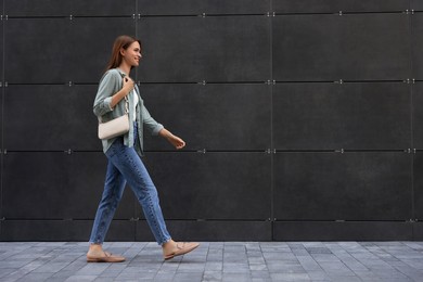 Photo of Young woman in casual clothes walking near grey wall outdoors, space for text