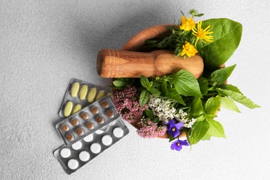 Wooden mortar with fresh herbs, flowers and pills on white table, flat lay