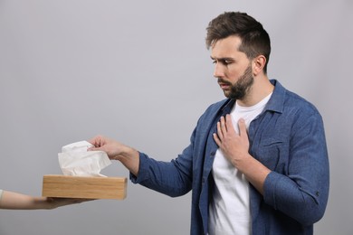 Sick man taking tissue on grey background. Cold symptoms