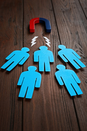 Magnet attracting paper people on wooden background