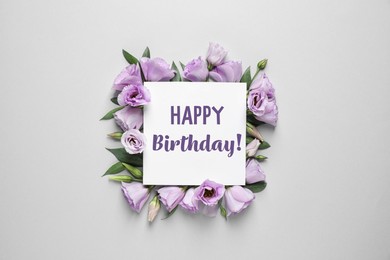 Image of Beautiful flowers and card with text Happy Birthday! on grey background, flat lay