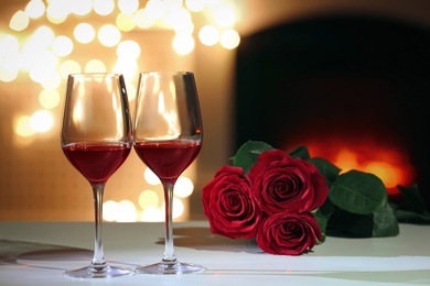 Glasses of wine and flowers on table against blurred lights. Romantic dinner