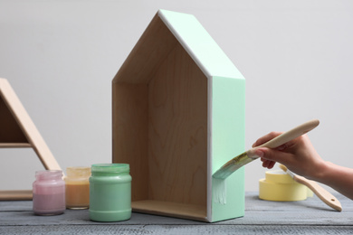 Woman painting wooden house model at grey table, closeup