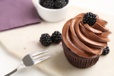 Delicious chocolate cupcake with cream and blackberries on white board, closeup