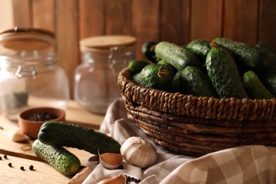 Photo of Fresh cucumbers and other ingredients near jars prepared for canning on wooden table