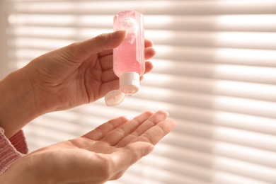 Woman applying antiseptic gel near window indoors, closeup