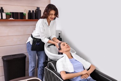 Professional hairdresser washing woman's hair in beauty salon