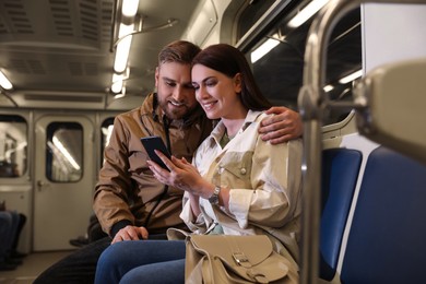 Happy couple using mobile phone in subway train. Public transport