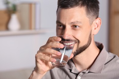 Photo of Happy man drinking water indoors. Refreshing drink