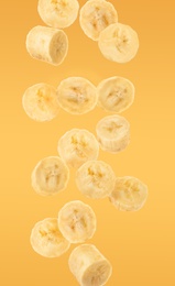 Slices of tasty ripe banana falling on yellow background