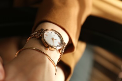 Photo of Woman wearing luxury wristwatch near mirror, closeup
