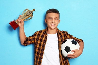 Happy boy with golden winning cup and soccer ball on blue background