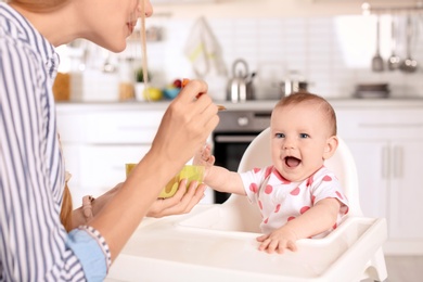 Woman feeding her child in highchair indoors. Healthy baby food
