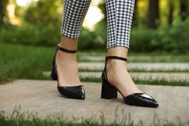 Photo of Woman in stylish black shoes walking at park, closeup