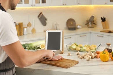 Man cutting chicken fillet while watching online cooking course via tablet in kitchen, closeup