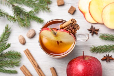 Hot mulled cider, ingredients and fir branches on white wooden table, flat lay