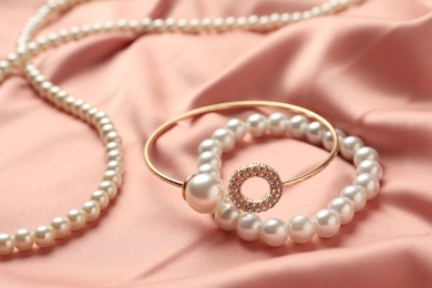 Photo of Elegant necklace and bracelets with pearls on pink silk, closeup