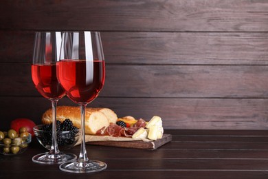 Photo of Glasses of delicious rose wine and snacks on wooden table, space for text